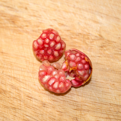 Dwarf red pomegranate split into three pieces on a wooden surface